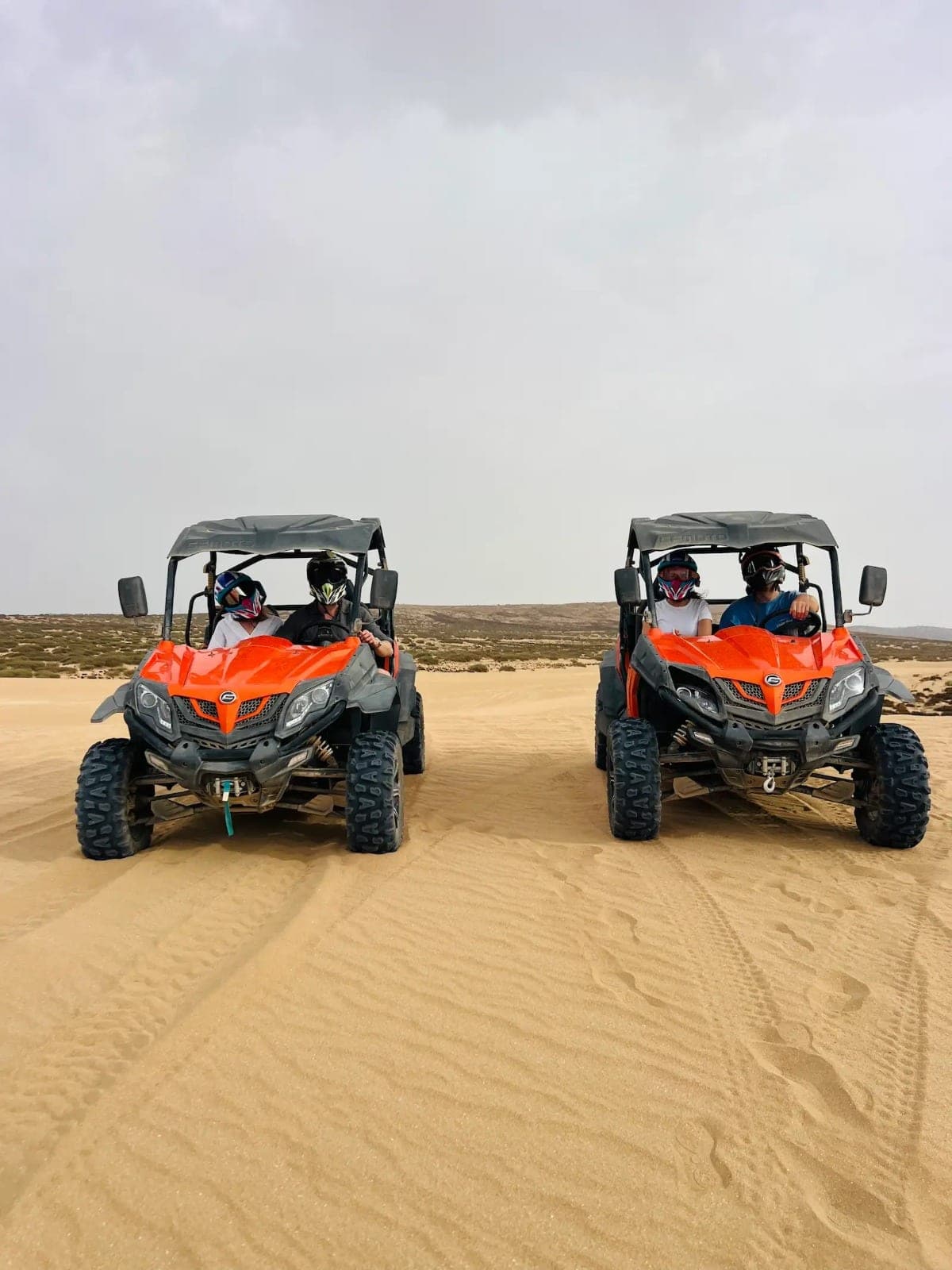 Two orange dune buggies with helmeted riders side by side on the sand at Timlalin