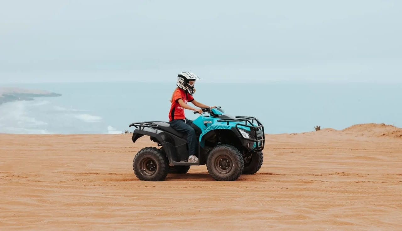Quad rider crossing a sandy plateau above the Atlantic coast during a Timlalin dunes tour near Agadir