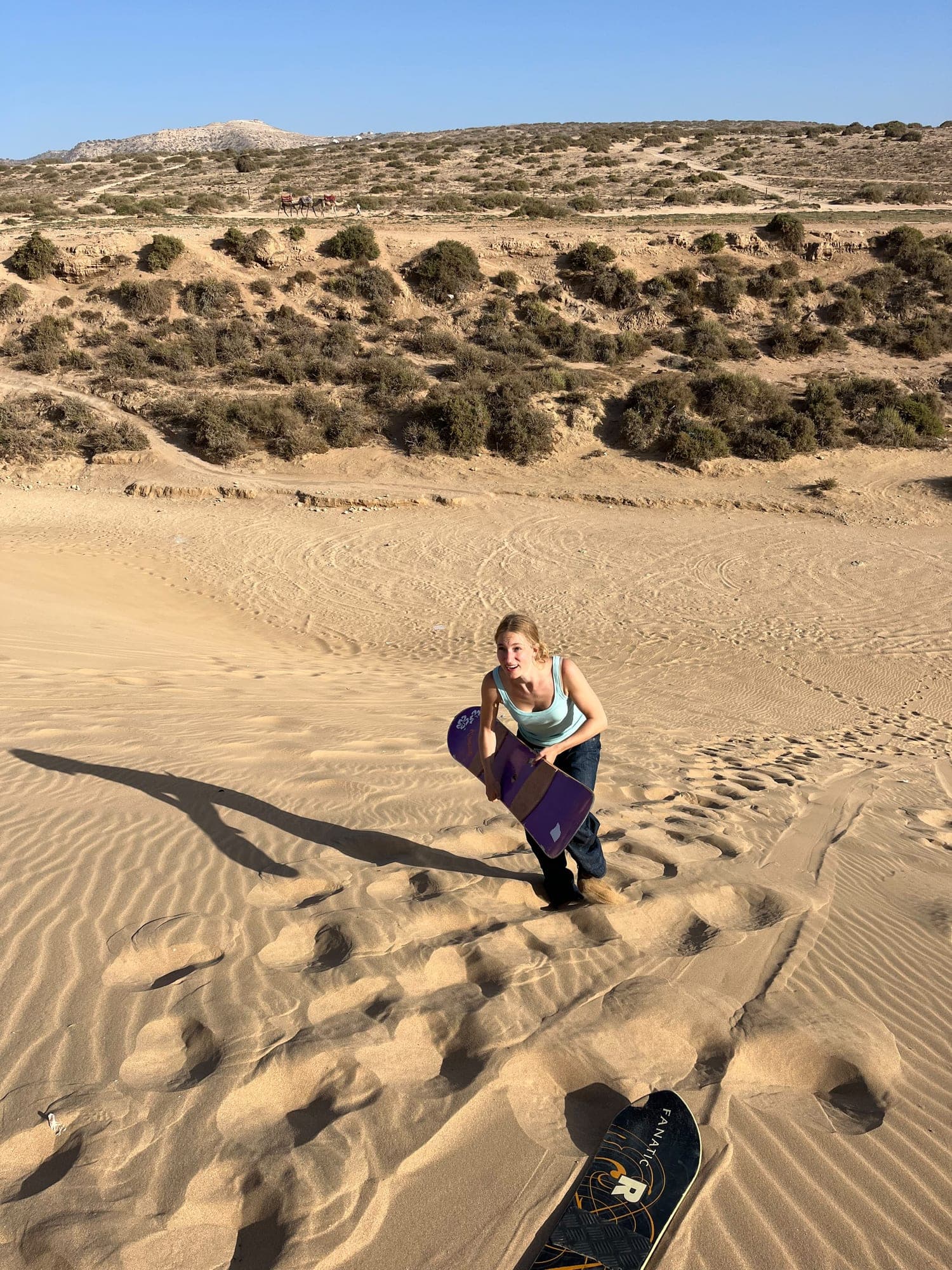Visitor climbing back up a sand dune with a sandboard in the Timlalin dunes